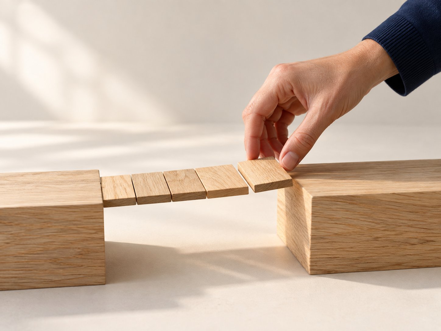 Eine Hand legt das letzte Brett einer kleinen Holzbrücke zwischen zwei Holzblöcken