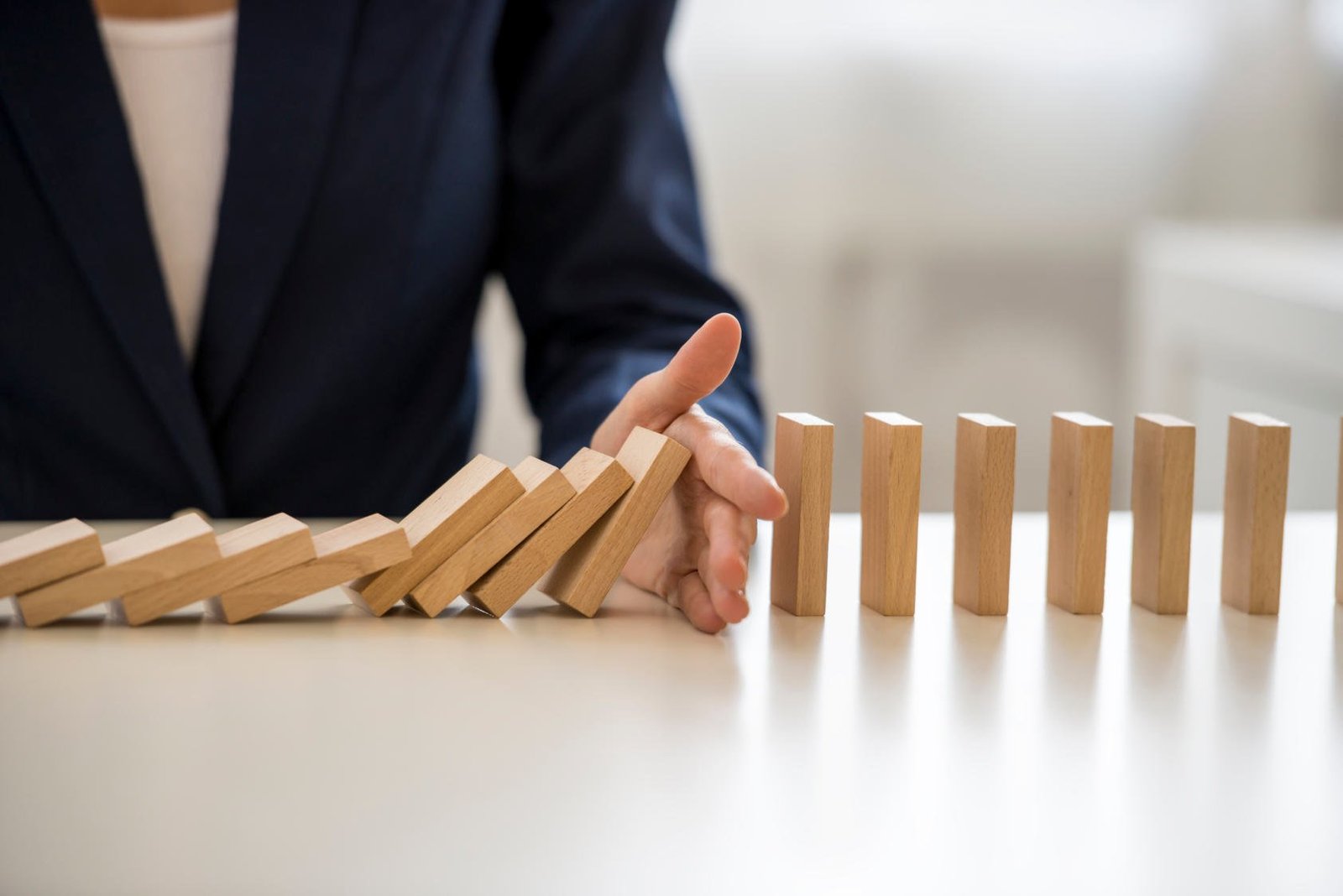 Hand stoppt eine Reihe fallender Dominosteine